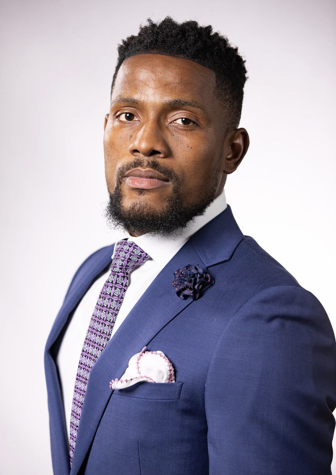 Portrait of Jonah Okebulu in a blue suit with a patterned tie.